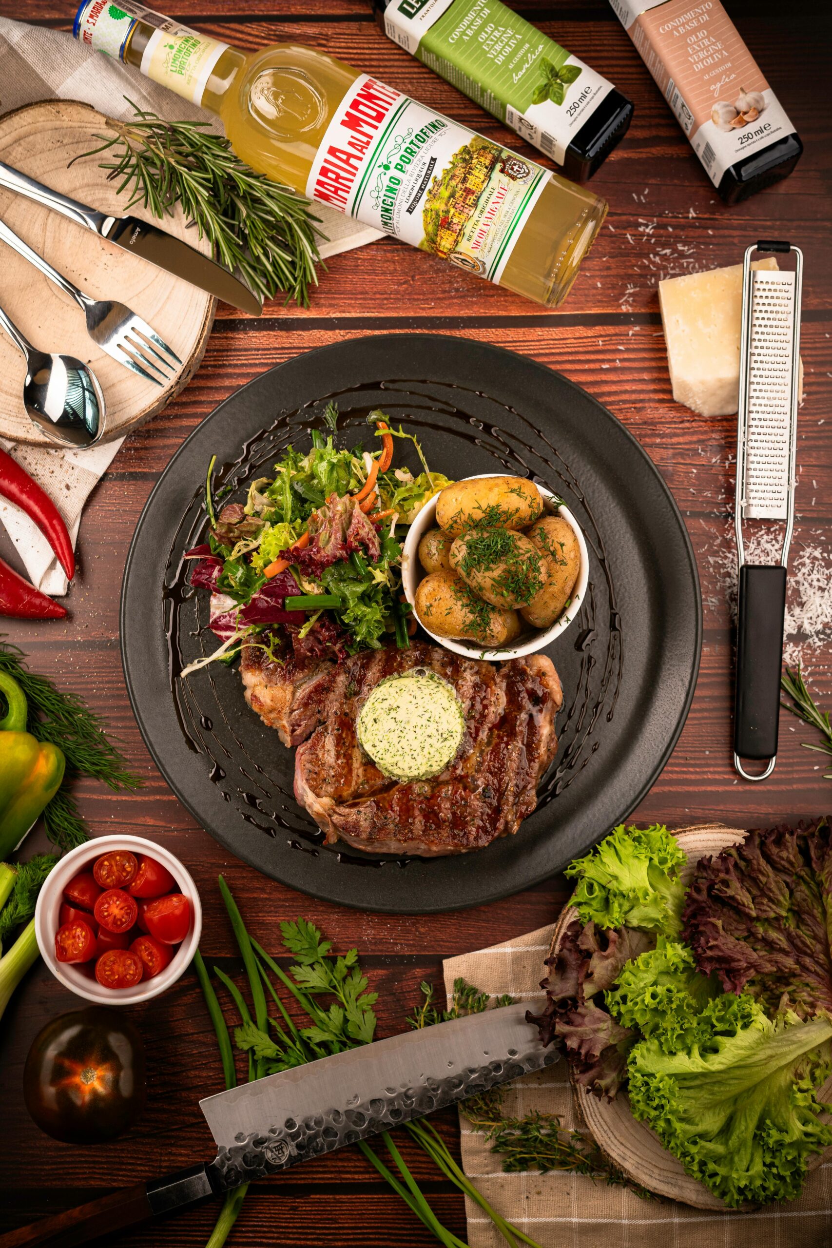 A delicious steak meal with salad, potatoes, and fresh ingredients on a wooden table.